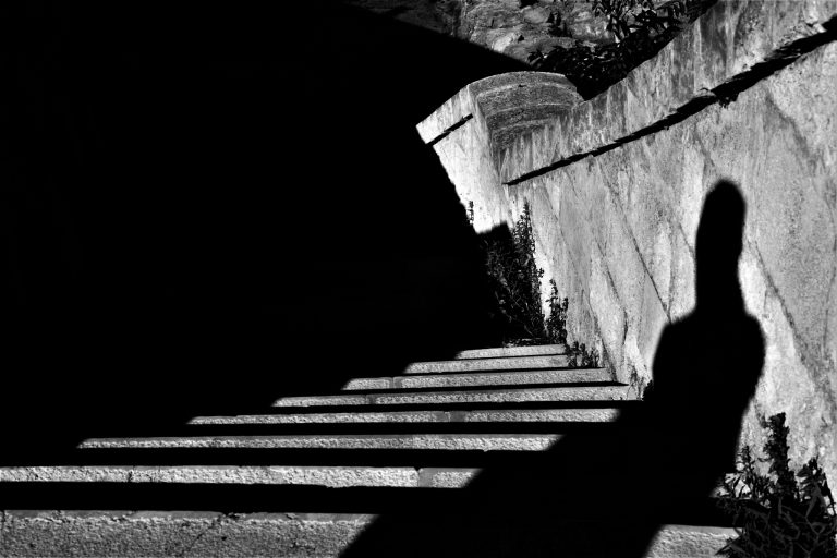 The shadow of a thoughtful man walking down the stairs in a black and white picture